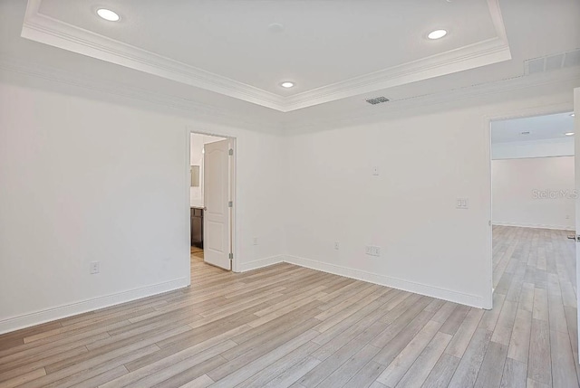 empty room featuring a tray ceiling, light hardwood / wood-style flooring, and ornamental molding