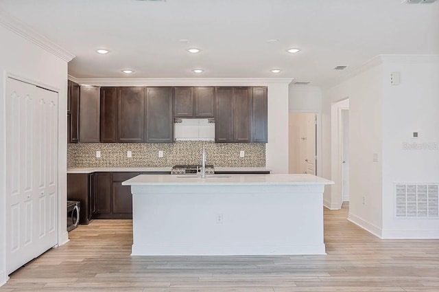 kitchen with dark brown cabinets, a center island with sink, and light hardwood / wood-style flooring