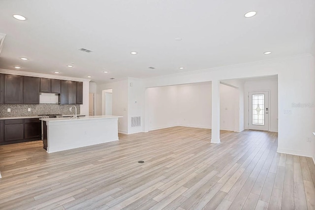 kitchen with tasteful backsplash, light hardwood / wood-style flooring, ornamental molding, and an island with sink