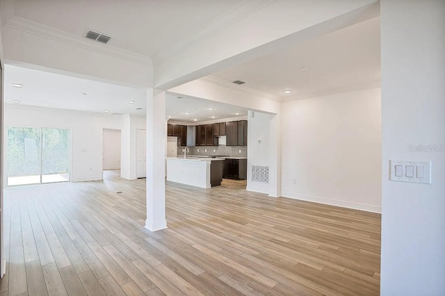 unfurnished living room with sink, crown molding, and light hardwood / wood-style floors