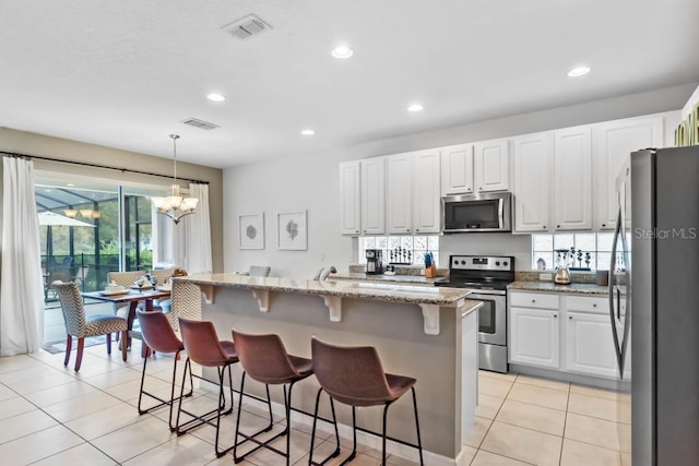 kitchen featuring light tile patterned floors, white cabinets, stainless steel appliances, light stone countertops, and a kitchen bar