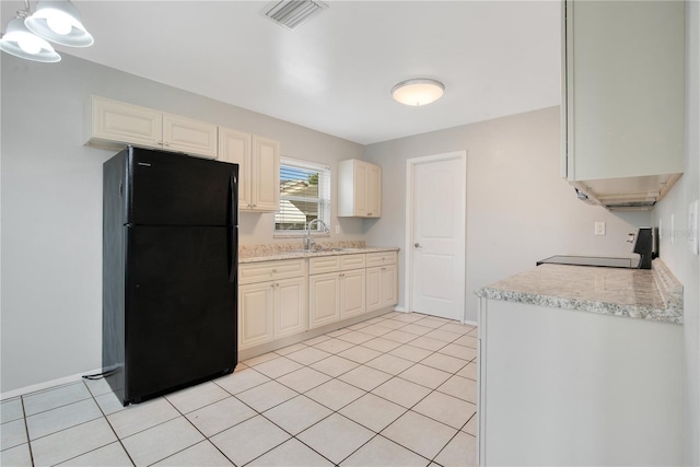 kitchen featuring stove, light tile patterned floors, black fridge, and sink