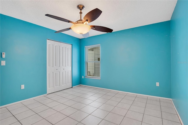 unfurnished bedroom featuring ceiling fan, a closet, light tile patterned floors, and a textured ceiling