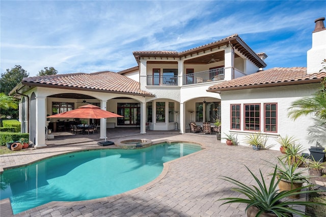 back of house with a swimming pool with hot tub, ceiling fan, a balcony, and a patio