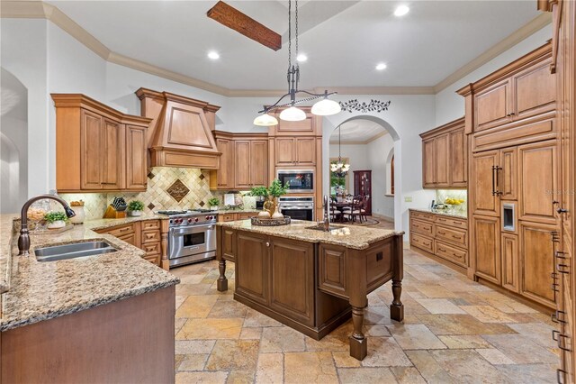 kitchen featuring sink, stainless steel appliances, light stone counters, premium range hood, and pendant lighting