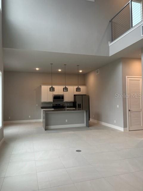 kitchen featuring pendant lighting, stainless steel appliances, light tile flooring, a towering ceiling, and a kitchen island with sink