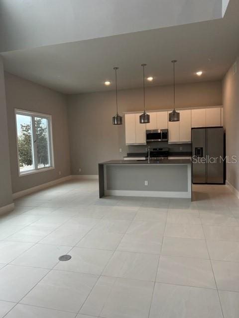 kitchen featuring light tile floors, appliances with stainless steel finishes, pendant lighting, and a kitchen island with sink