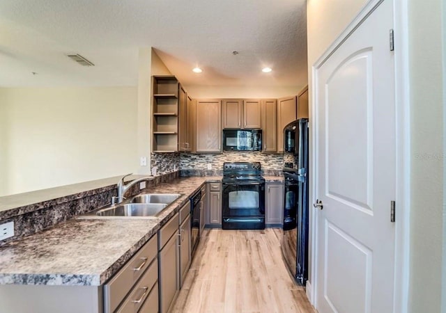 kitchen with black appliances, kitchen peninsula, sink, light hardwood / wood-style flooring, and a textured ceiling