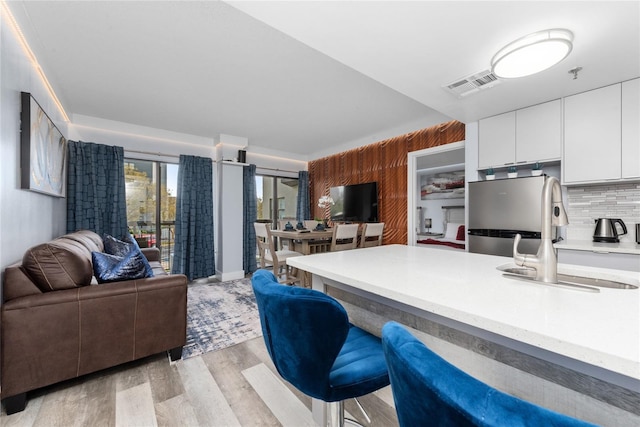 kitchen featuring stainless steel fridge, tasteful backsplash, light hardwood / wood-style flooring, white cabinets, and sink