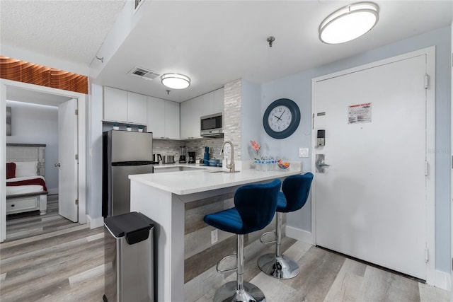 kitchen with sink, white cabinets, backsplash, light hardwood / wood-style floors, and stainless steel appliances