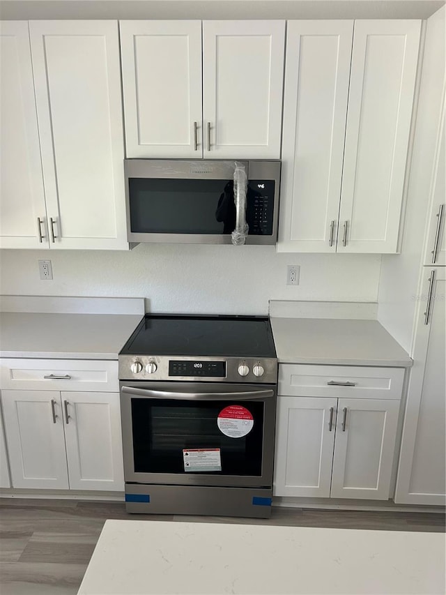 7539 Bernal Dr, Sebring, FL 33872 - kitchen with stainless steel appliances, light countertops, white cabinets, and light wood finished floors