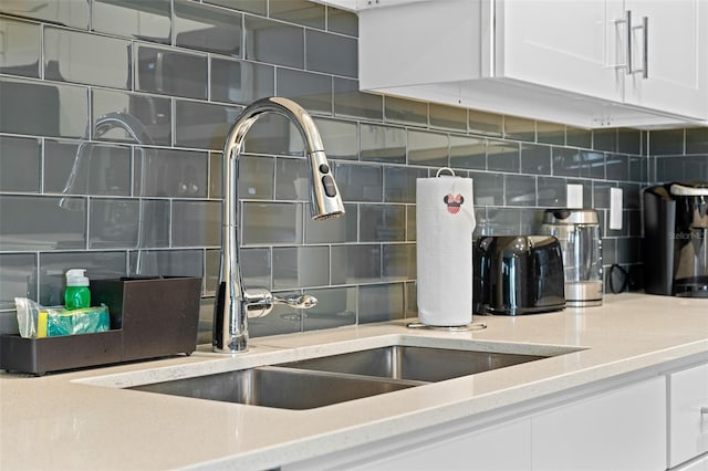 interior details featuring light stone counters, tasteful backsplash, a sink, and white cabinetry