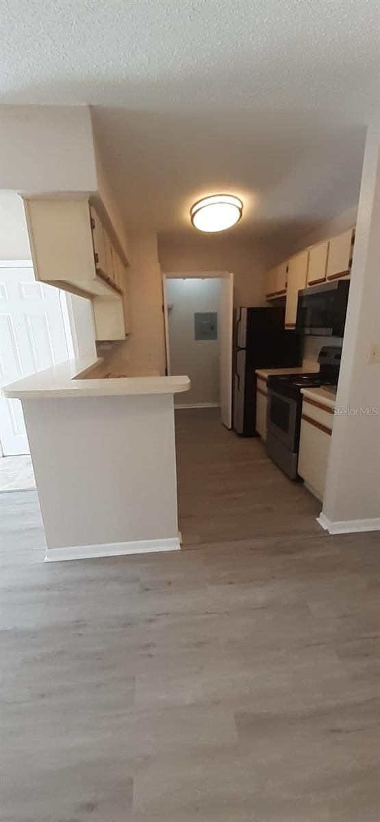 kitchen with kitchen peninsula, electric range, light hardwood / wood-style floors, and a textured ceiling