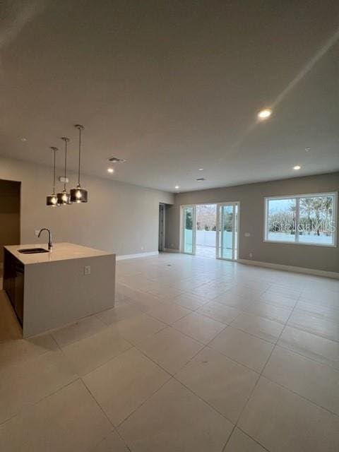 interior space featuring light tile flooring, a center island with sink, decorative light fixtures, and sink