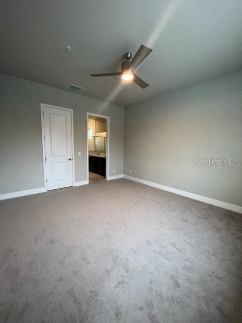 unfurnished bedroom with ensuite bath, dark colored carpet, and ceiling fan