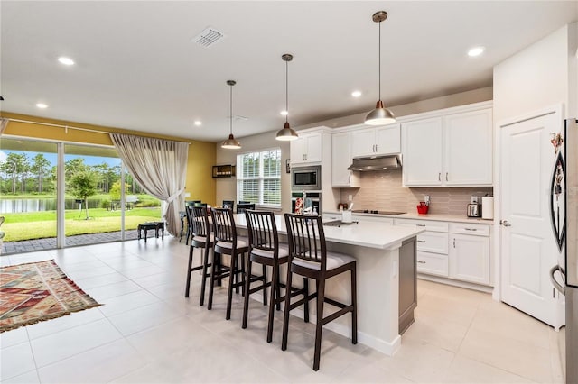 kitchen featuring decorative backsplash, appliances with stainless steel finishes, white cabinets, hanging light fixtures, and an island with sink