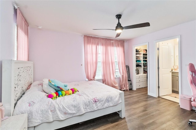 bedroom with ensuite bathroom, a walk in closet, ceiling fan, wood-type flooring, and a closet