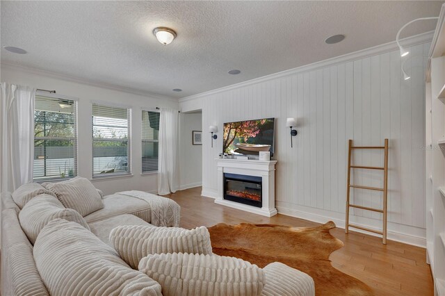 living area with a textured ceiling, baseboards, ornamental molding, light wood finished floors, and a glass covered fireplace