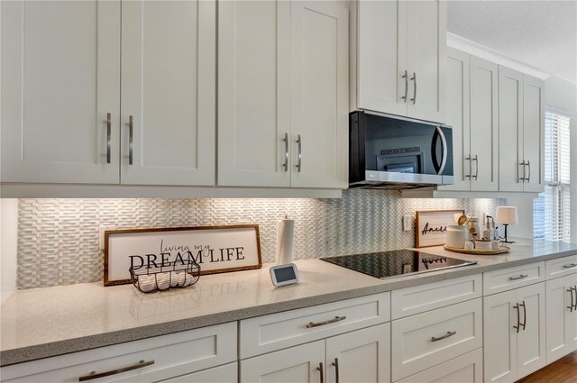 kitchen with tasteful backsplash, white cabinets, stainless steel microwave, light stone countertops, and black electric cooktop