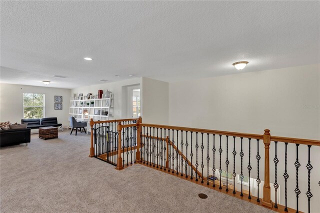 hall featuring a textured ceiling, carpet, and an upstairs landing