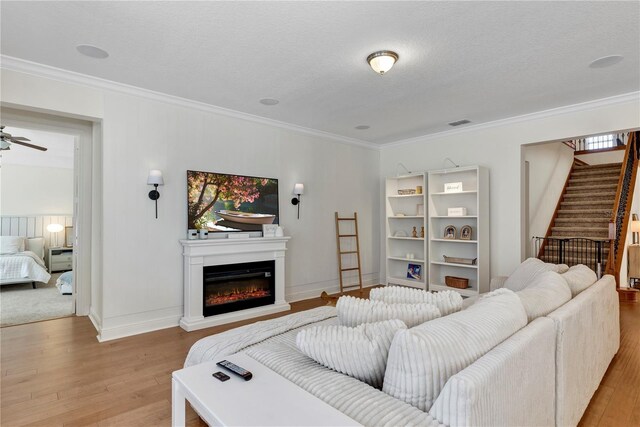 living area featuring ornamental molding, stairway, a glass covered fireplace, and light wood-style flooring