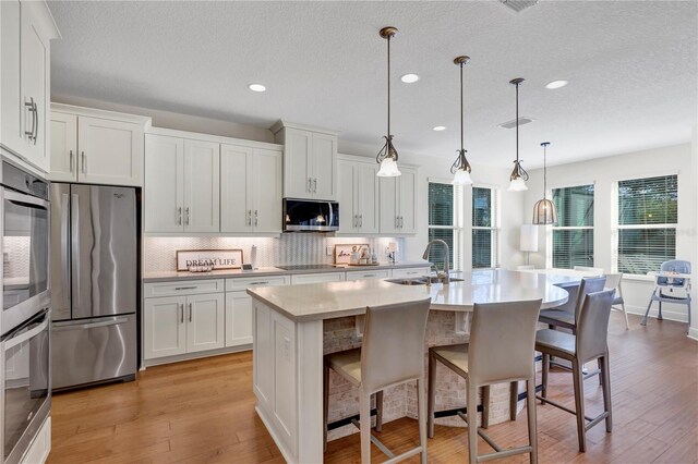 kitchen featuring sink, stainless steel appliances, an island with sink, white cabinets, and decorative light fixtures