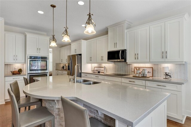 kitchen featuring a sink, white cabinetry, appliances with stainless steel finishes, an island with sink, and decorative light fixtures