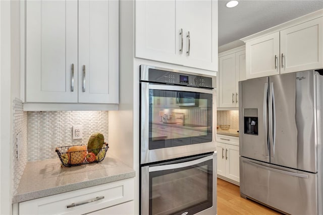 kitchen featuring appliances with stainless steel finishes, tasteful backsplash, white cabinetry, light stone countertops, and light hardwood / wood-style flooring