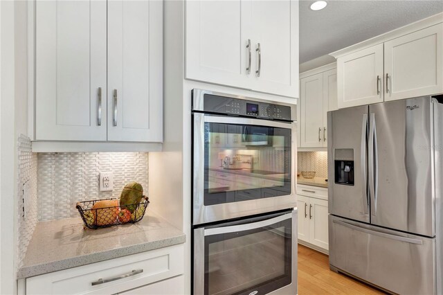 kitchen with light stone counters, stainless steel appliances, tasteful backsplash, white cabinetry, and light wood-type flooring