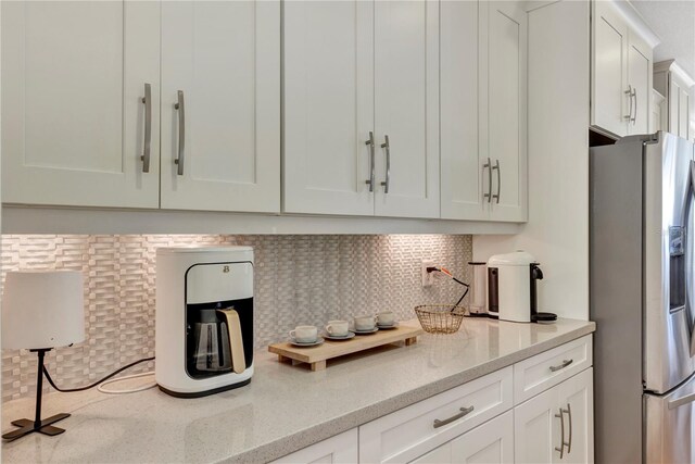 kitchen featuring tasteful backsplash, light stone counters, stainless steel fridge, and white cabinets