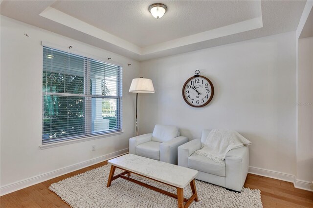 living area with a textured ceiling, a tray ceiling, wood finished floors, and baseboards