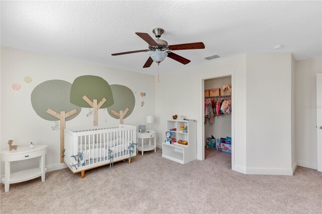 carpeted bedroom featuring a nursery area, a spacious closet, ceiling fan, a textured ceiling, and a closet