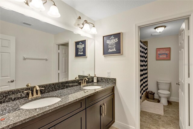 full bath featuring baseboards, a sink, toilet, and double vanity