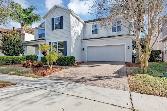 traditional-style house featuring a garage, decorative driveway, and stucco siding