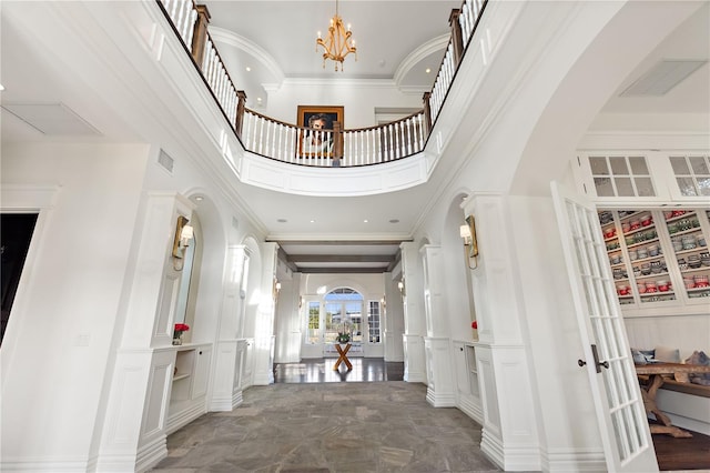 foyer featuring french doors, a high ceiling, an inviting chandelier, and crown molding