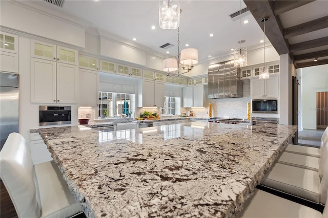 kitchen with a large island, hanging light fixtures, built in appliances, light stone countertops, and white cabinetry