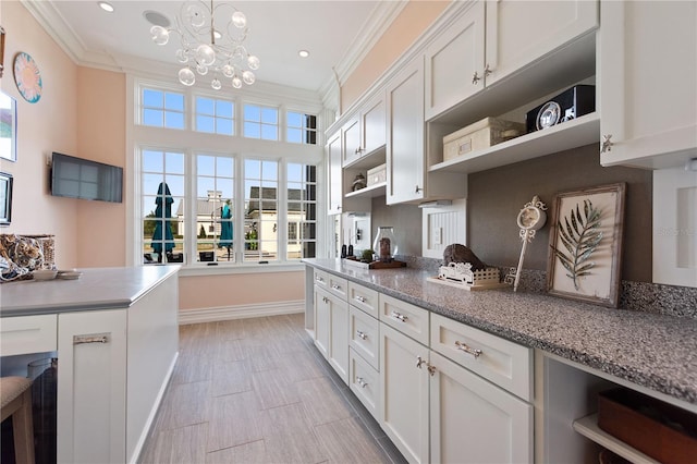 kitchen with white cabinetry, light stone counters, ornamental molding, hanging light fixtures, and a chandelier