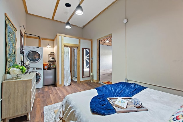bedroom with stacked washing maching and dryer, fridge, and hardwood / wood-style floors