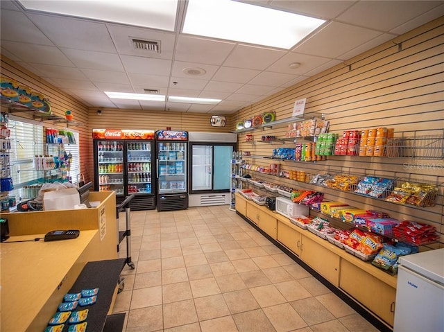 interior space featuring light tile patterned flooring, wooden walls, refrigerator, and a paneled ceiling