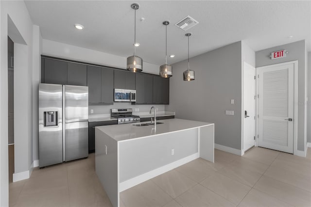 kitchen with an island with sink, stainless steel appliances, sink, pendant lighting, and a textured ceiling