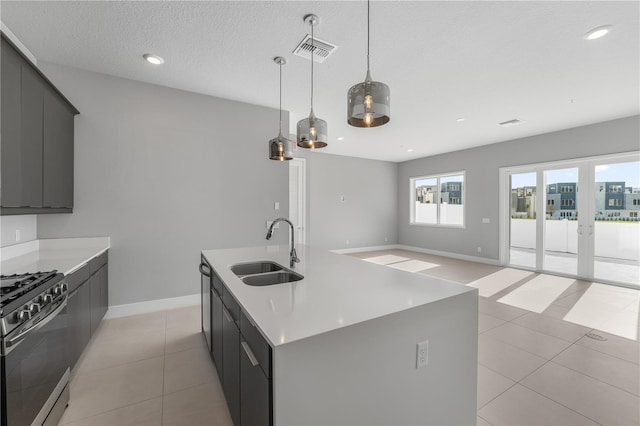 kitchen with a kitchen island with sink, decorative light fixtures, sink, appliances with stainless steel finishes, and a textured ceiling