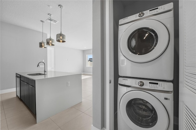 washroom featuring light tile patterned floors, sink, stacked washer / drying machine, and a textured ceiling