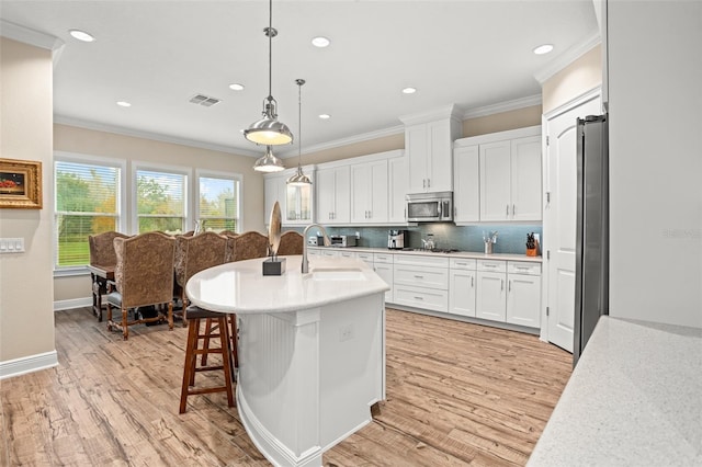 kitchen featuring tasteful backsplash, a kitchen island with sink, pendant lighting, light hardwood / wood-style floors, and white cabinetry