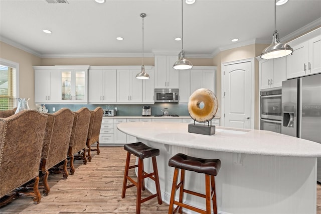 kitchen featuring white cabinetry, stainless steel appliances, hanging light fixtures, and light hardwood / wood-style flooring