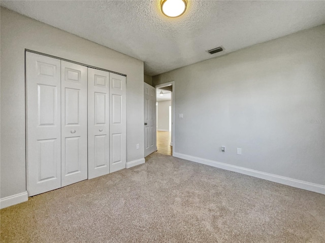 unfurnished bedroom featuring a closet, light colored carpet, and a textured ceiling