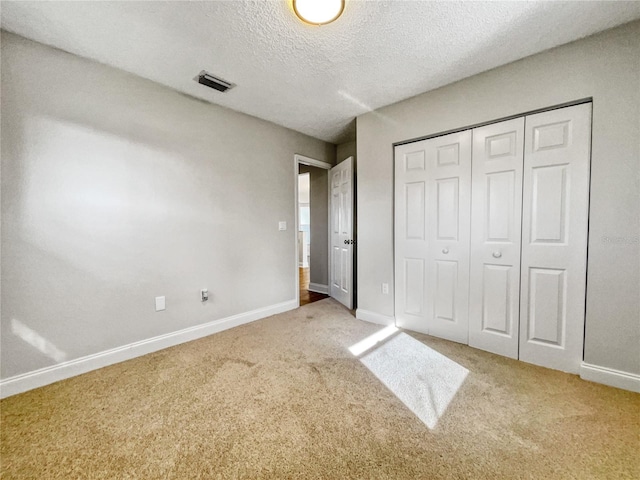 unfurnished bedroom with light carpet, a textured ceiling, and a closet