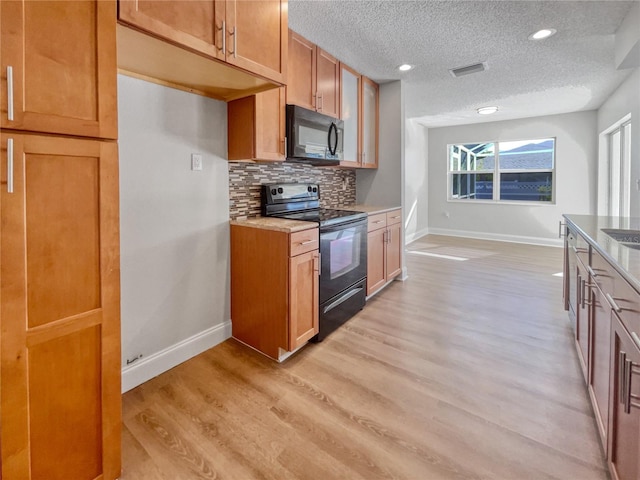 kitchen featuring light wood-type flooring, a textured ceiling, backsplash, and black appliances