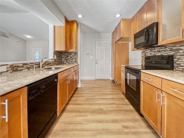 kitchen featuring light stone countertops, sink, light hardwood / wood-style floors, a textured ceiling, and black appliances