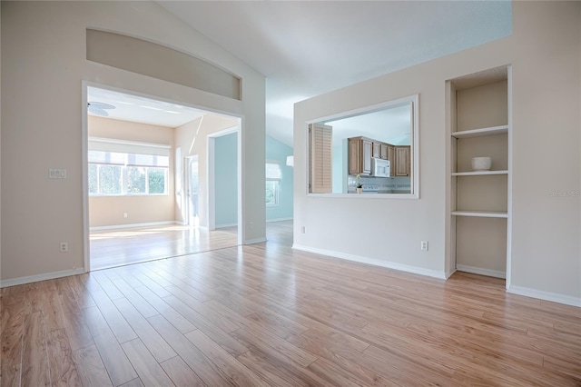 unfurnished living room with lofted ceiling, light wood-type flooring, and built in shelves