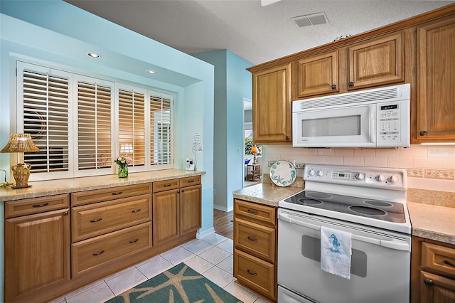 kitchen with tasteful backsplash, light tile patterned floors, white appliances, and light stone counters